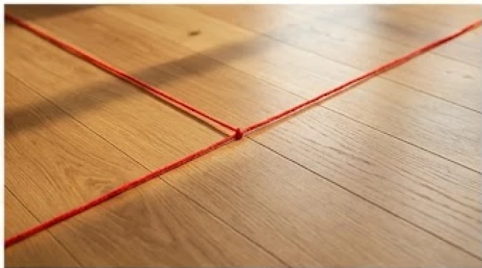 Một sợi dây đỏ được kéo căng trên mặt sàn gỗ để đánh dấu ranh giới các cung vị phong thủy trong ngôi nhà