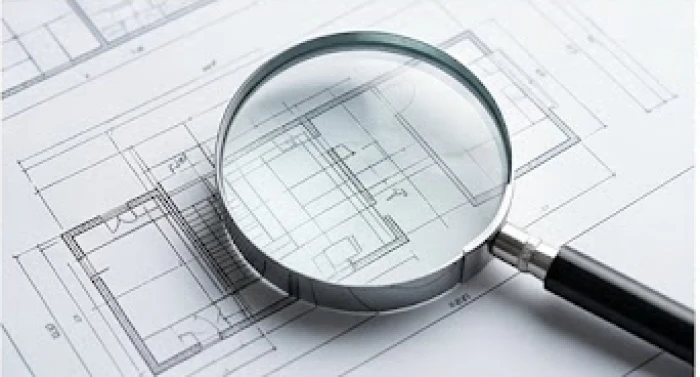 Kính lúp soi chiếu chi tiết nhỏ trên một bản vẽ kiến trúc thể hiện sự cầu toàn thái quá và áp lực hoàn hảo