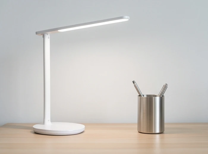 Đèn học LED ánh sáng trắng và ống đựng bút màu ghi sáng được sắp xếp ngăn nắp trên mặt bàn gỗ