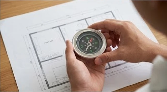 Bàn tay cầm chiếc la bàn định vị chính xác góc độ hướng bắc thực tế trên một mặt bằng căn hộ chung cư