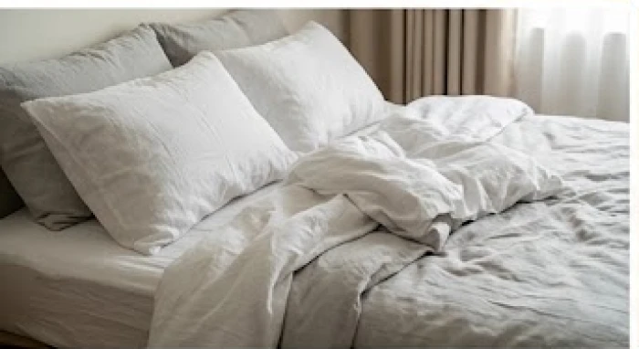 Chiếc giường ngủ được trải bộ ga gối màu xám nhạt và trắng tinh tươm trong không gian tối giản