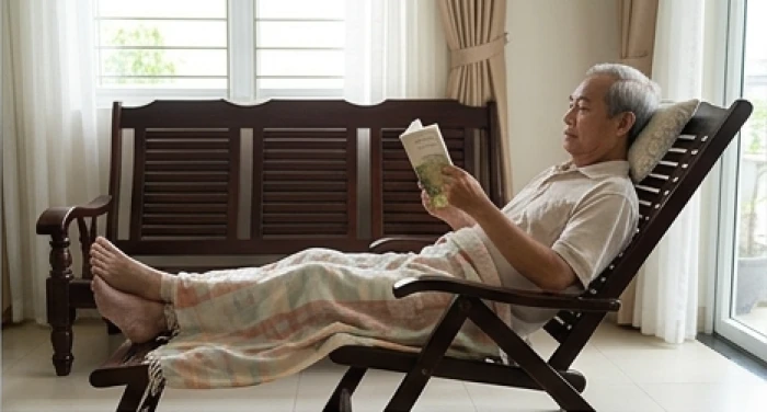 Cụ ông ngồi nghỉ ngơi trên ghế tựa với dáng vẻ thư thái và chiếc chăn mỏng đắp ngang chân