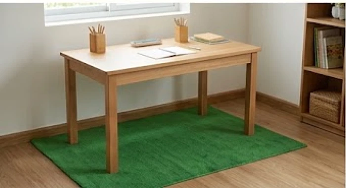 Tấm thảm nhỏ màu xanh lá cây trải gọn gàng dưới chân chiếc bàn học gỗ