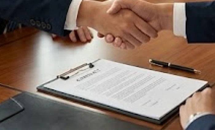 Hai người đối tác đang bắt tay nhau ký kết hợp đồng kinh doanh thành công trên chiếc bàn gỗ lớn sang trọng