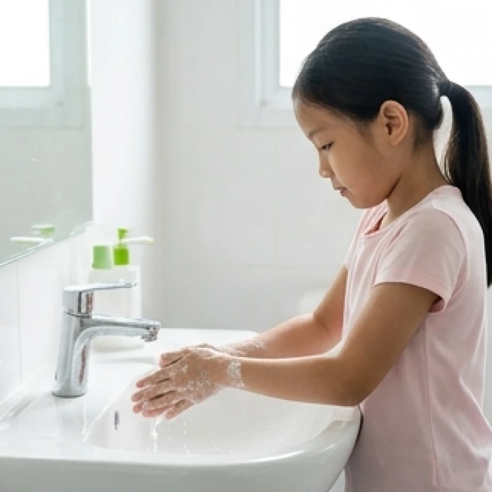 Bé gái đang cẩn thận rửa tay bằng xà phòng dưới vòi nước sạch tại bồn rửa mặt trong nhà vệ sinh
