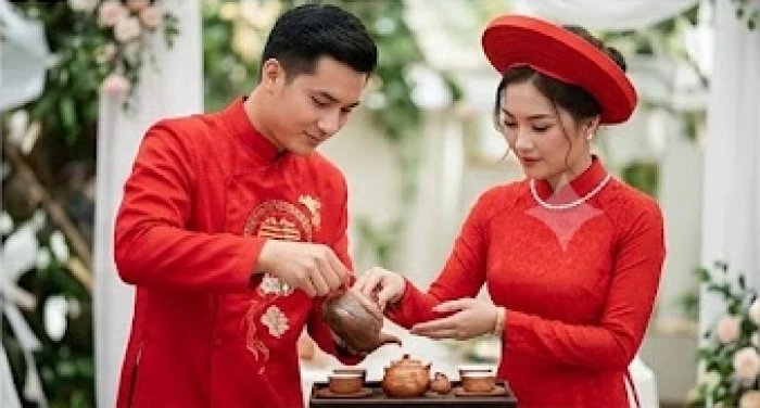 Cô dâu chú rể trong trang phục áo dài cưới truyền thống màu đỏ đang thực hiện nghi thức rót trà
