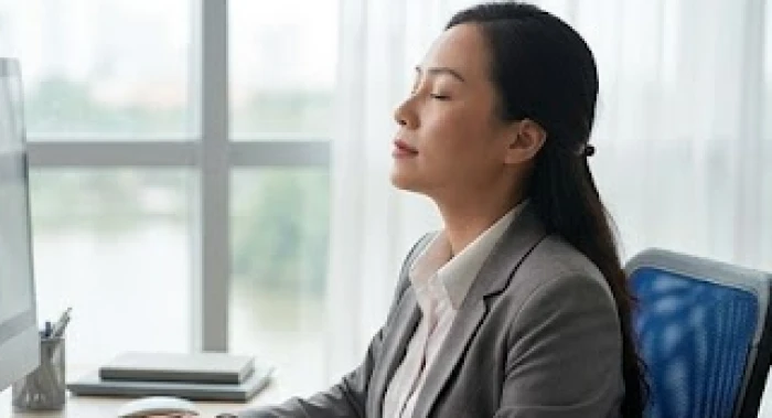 Người phụ nữ tuổi Tuất nhắm mắt hít thở sâu tại góc làm việc để kiểm soát tính cách nữ tuổi tuất bướng bỉnh