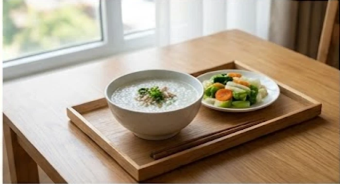 Khay thức ăn với các món rau củ luộc mềm và bát cháo nóng hổi đặt trên bàn ăn bằng gỗ