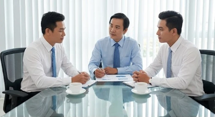 Ba vị giám đốc cùng thảo luận dự án trên bàn kính văn phòng áp dụng phương pháp mượn tuổi làm ăn chung.