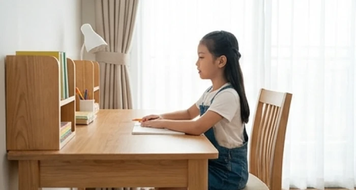 Bé gái ngồi thẳng lưng tại bàn học hướng mặt về phương vị diên niên tốt lành với ánh sáng tràn ngập