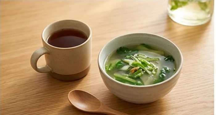 Tách nước đỗ đen rang ấm áp cùng bát canh rau xanh thanh mát bày biện trên bàn ăn gia đình