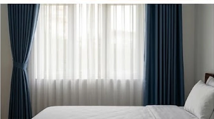 Khung cửa sổ được che chắn bởi rèm vải hai lớp màu xanh dương đậm kết hợp với voan trắng mềm mại