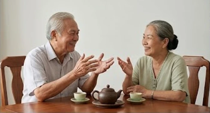 Hai người lớn tuổi ngồi trò chuyện vui vẻ bên bộ ấm trà bằng gốm sứ tượng trưng cho sự hòa thuận bộ tam hợp
