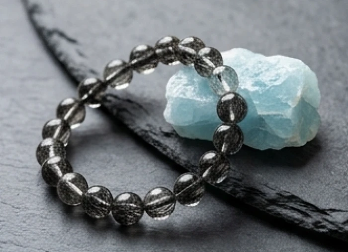 Vòng tay thạch anh tóc đen mật độ rutile dày đặt cạnh viên đá ngọc xanh biển aquamarine
