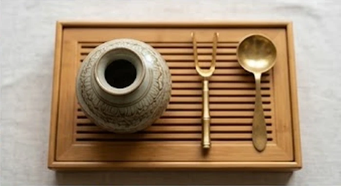 Bình gốm sứ tinh xảo đặt cạnh bộ dụng cụ pha trà bằng đồng thau minh họa cho sự tương sinh thổ sinh kim.