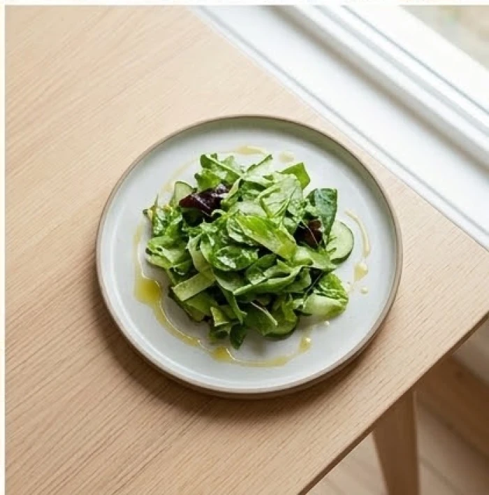 Đĩa salad rau xanh tươi mát rưới dầu ô liu được đặt ngay ngắn trên bàn ăn gỗ mang lại cảm giác thanh nhẹ