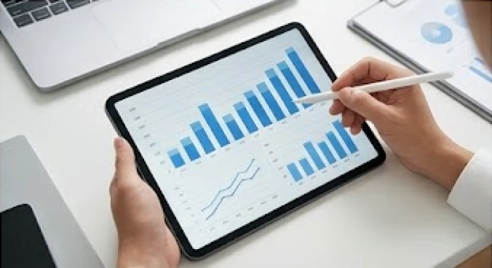 Bàn tay cầm bút chỉ vào các biểu đồ cột tăng trưởng trên máy tính bảng để minh họa cho một lập luận phân tích