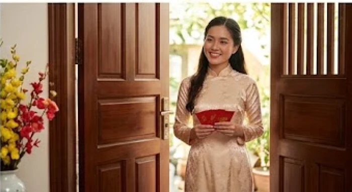 Người khách mặc áo dài tươi cười bước vào nhà chúc Tết gia chủ trong dịp đầu năm mới