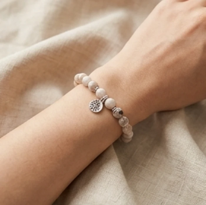 Cổ tay thanh mảnh của nữ giới đeo chiếc vòng đá phong thủy cỡ 10mm phối cùng charm bạc nhỏ