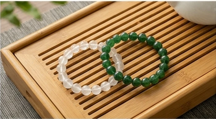 Hai mẫu vòng tay thạch anh màu trắng xám cho mệnh kim và màu xanh lục cho mệnh mộc đặt cạnh nhau trên bàn trà